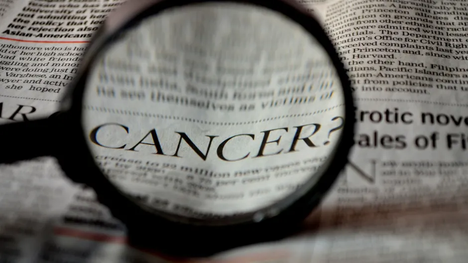 Das Wort "CANCER" in einer Zeitung wird durch eine Lupe hervorgehoben